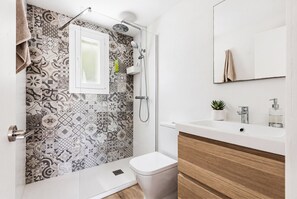 Un bagno con piastrelle decorate, un water, una doccia, un lavandino con uno specchio e una piccola pianta.