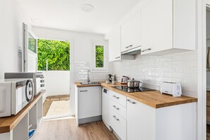 Une cuisine moderne avec des meubles blancs, un plan de travail en bois, un lave-vaisselle encastré et une fenêtre donnant sur un paysage verdoyant.
