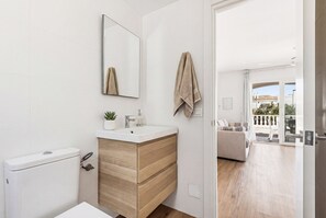 Une salle de bain moderne équipée de toilettes, d’un lavabo et d’un miroir, avec vue sur un balcon aménagé avec du mobilier d’extérieur.
