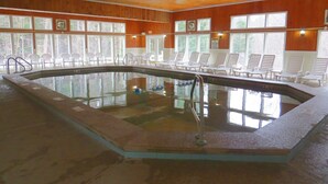 Une piscine intérieure aux murs recouverts de bois, entourée de chaises longues et dotée de grandes fenêtres.