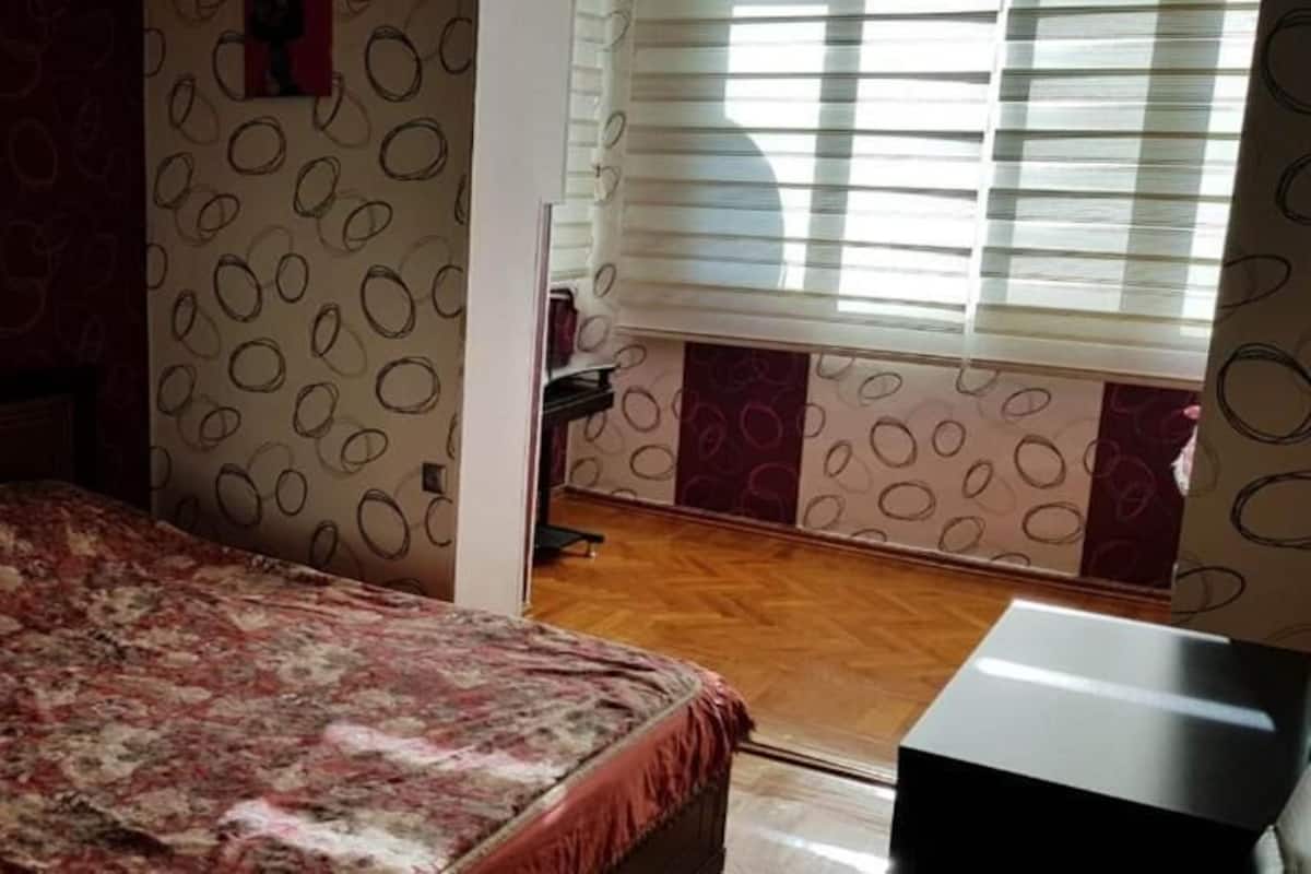 A bedroom with a bed, a desk, and a window with blinds.