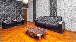 Habitació amb paper pintat, un sofà, dues butaques, una taula de centre i un llum penjant.