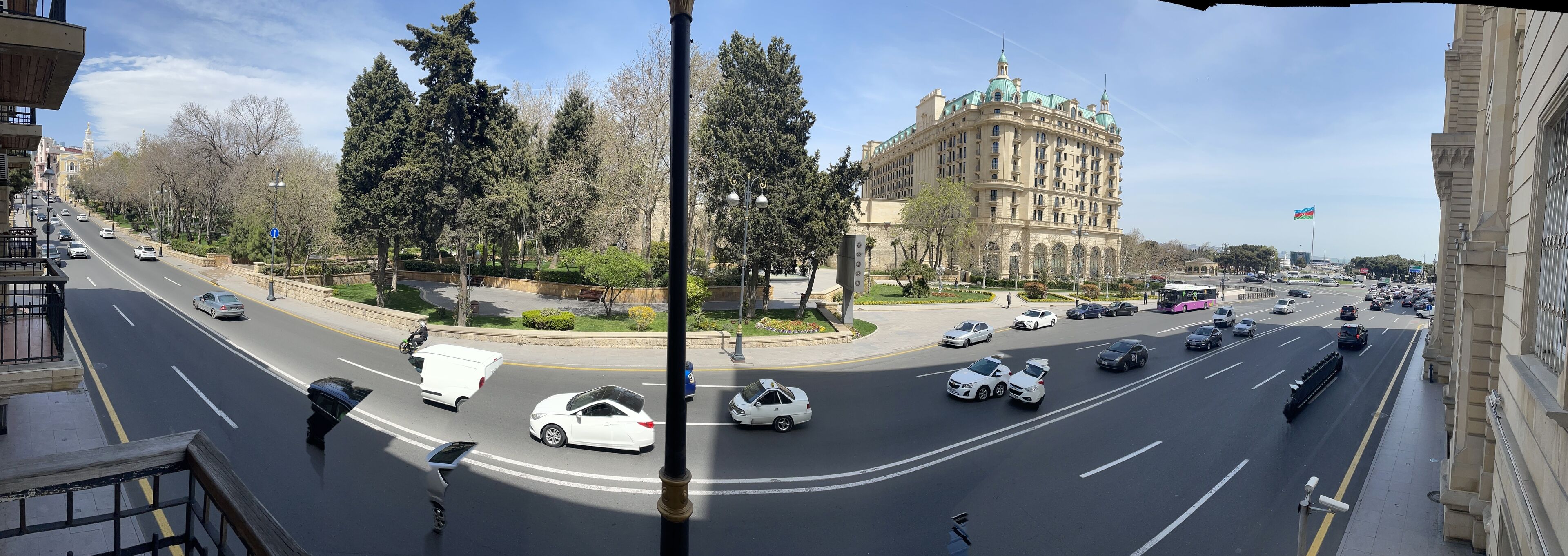 A multi-lane road with vehicles, a large building with classical architecture, and a flag.