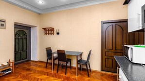 Zona de menjador amb taula i cadires, un sòl de fusta, una porta i un microones damunt d'una barra.