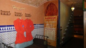 Una stanza con soffitto in mattoni, un letto, una parete con il cartello 'Peignoirs' e un poster con la scritta 'HAMMAM'.