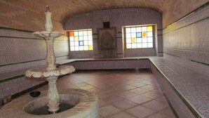 Una stanza piastrellata con una fontana al centro, pareti decorate e due finestre con vetrate colorate.