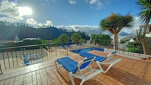 Une terrasse dotée de chaises longues et d’une piscine, entourée de verdure et avec une chaîne de montagnes en toile de fond.