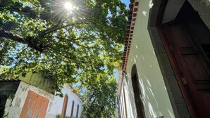 Une ruelle étroite, dallée de pierres, bordée de bâtiments aux portes en arc de cercle et d’un mur blanc orné d’une porte rouge.