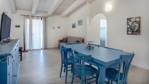 Un coin repas avec une table et des chaises bleues, un canapé et un téléviseur posé sur une commode.