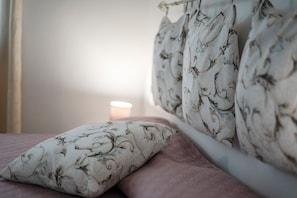 Un lit avec un oreiller et des rideaux à motifs floraux, une lampe de chevet et une fenêtre également dotée de rideaux.
