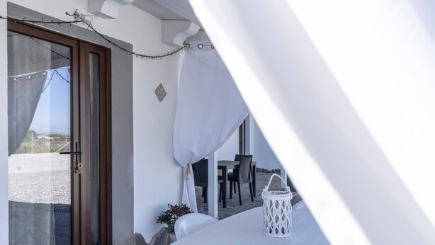 Une pièce avec une table blanche, une lanterne blanche, une porte avec un panneau de verre et une vue sur l’extérieur.
