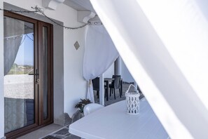 Une pièce avec une table blanche, une lanterne blanche, une porte avec un panneau de verre et une vue sur l’extérieur.