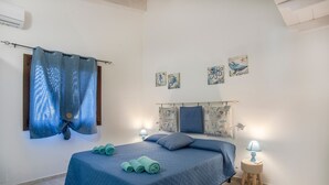 Une chambre à coucher avec un lit, des rideaux, des œuvres d’art au mur, une lampe de chevet et un petit tabouret.