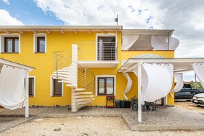 Un edificio amarillo con una escalera de caracol, un porche cubierto y un coche estacionado afuera.