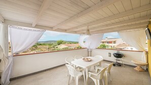Un balcon abrité, équipé d’une table et de chaises, d’un barbecue et offrant une vue sur les maisons.