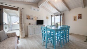 Une pièce comprenant une table à manger, des chaises, un canapé, un téléviseur et des œuvres d’art accrochées aux murs.