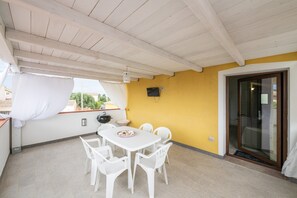 Un patio techado con una mesa y sillas, un televisor montado en la pared y un amplio ventanal corredero.