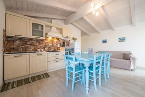 Eine Küche mit Steinrückwand, Holzschränken, einem Esstisch mit Stühlen und einem Sofa.