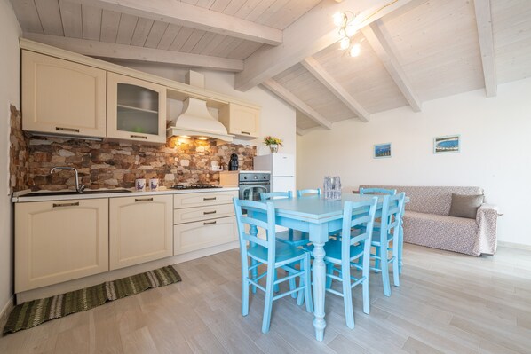 A kitchen with stone backsplash, wooden cabinets, a dining table with chairs, and a sofa.