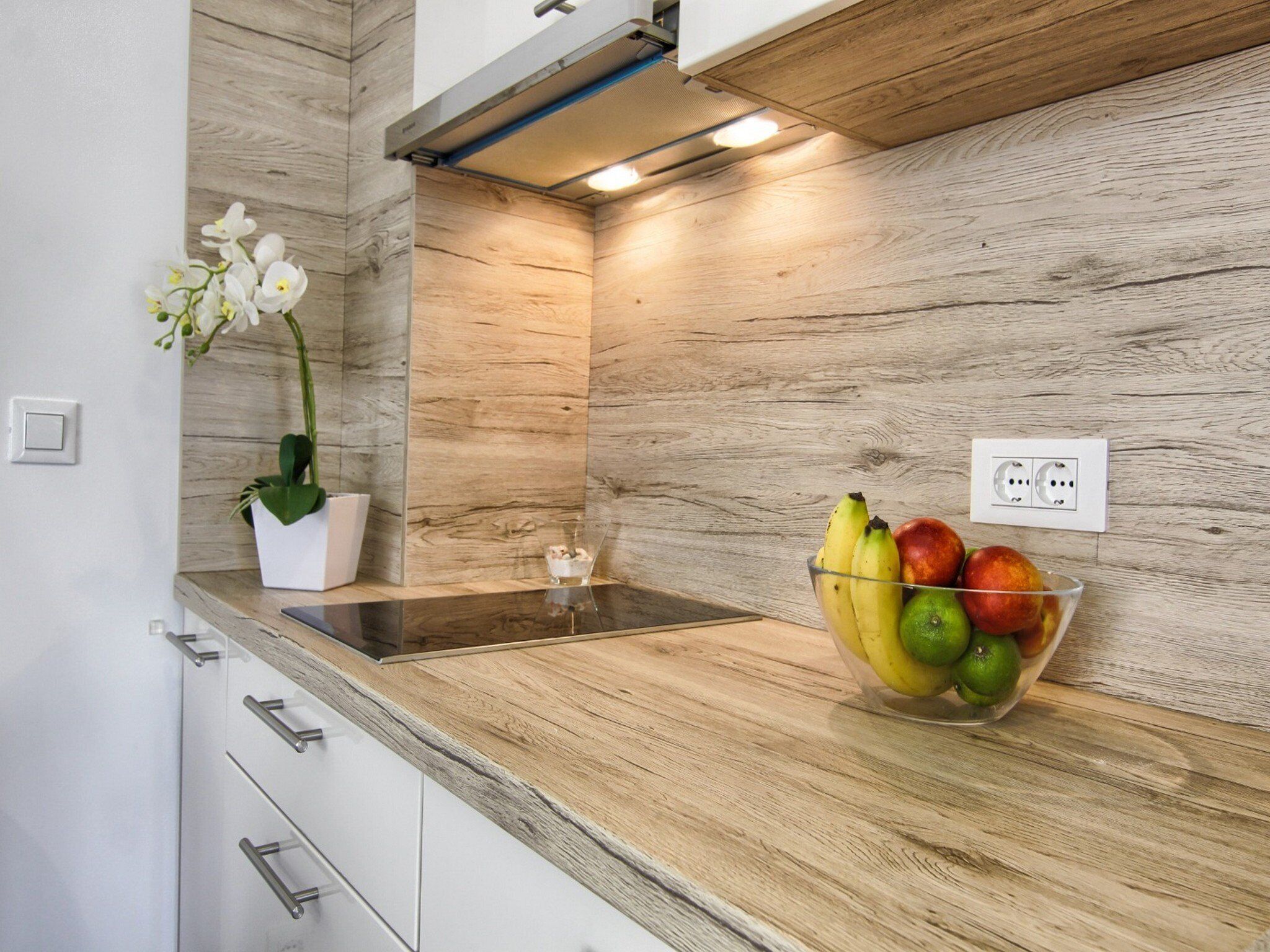 Una cocina con encimera de madera, un cuenco de fruta, una orquídea en maceta y una estufa moderna.