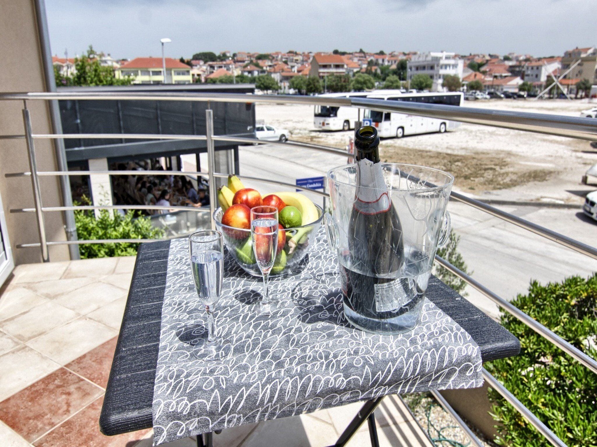 A balcony with a table set for a drink, a bottle of wine, and a bowl of fruit.