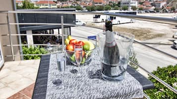 A balcony with a table set for a drink, a bottle of wine, and a bowl of fruit.