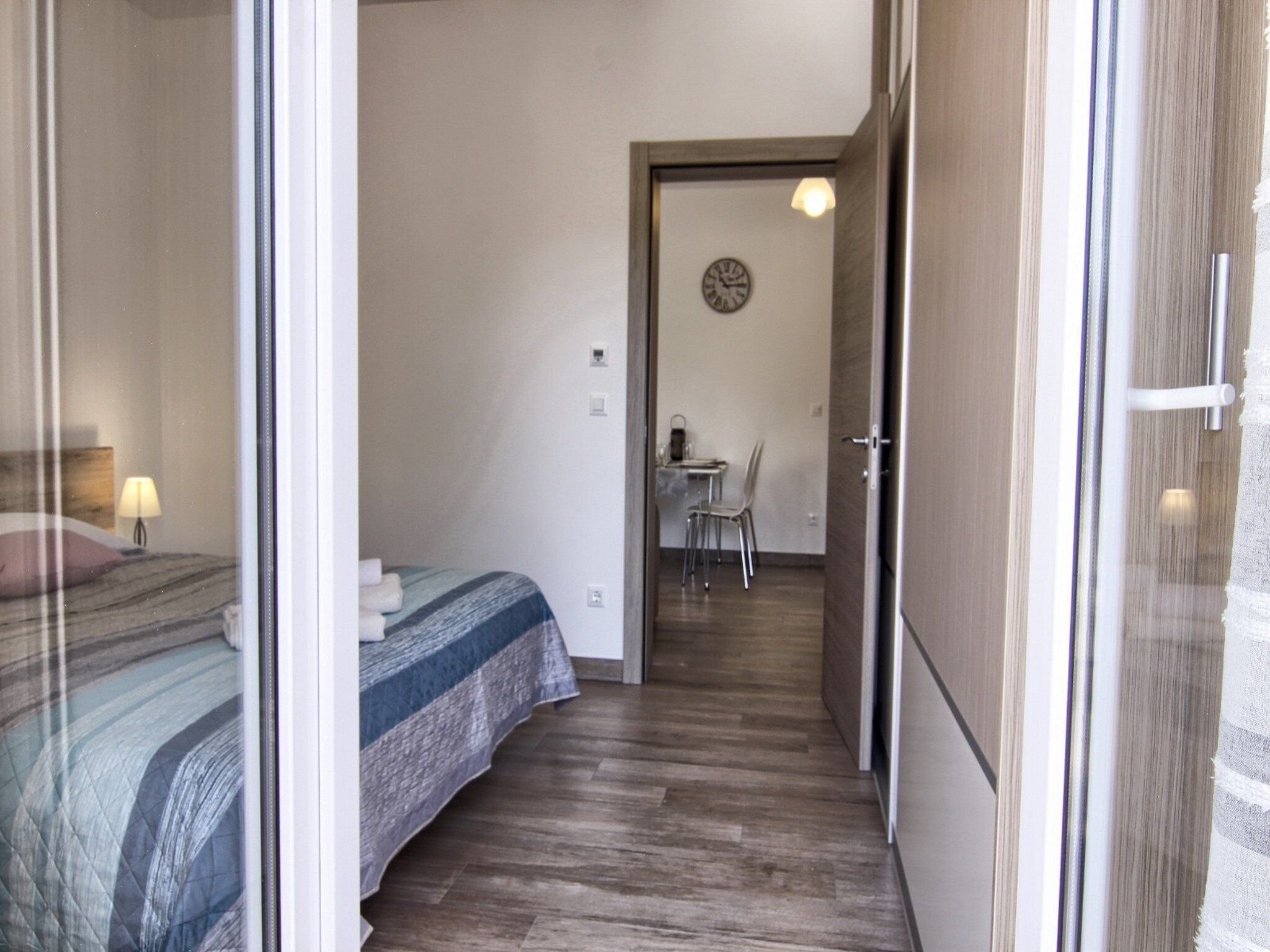 Un dormitorio con cama, una mesita de noche con lámpara, y una pequeña mesa con sillas en la habitación contigua.