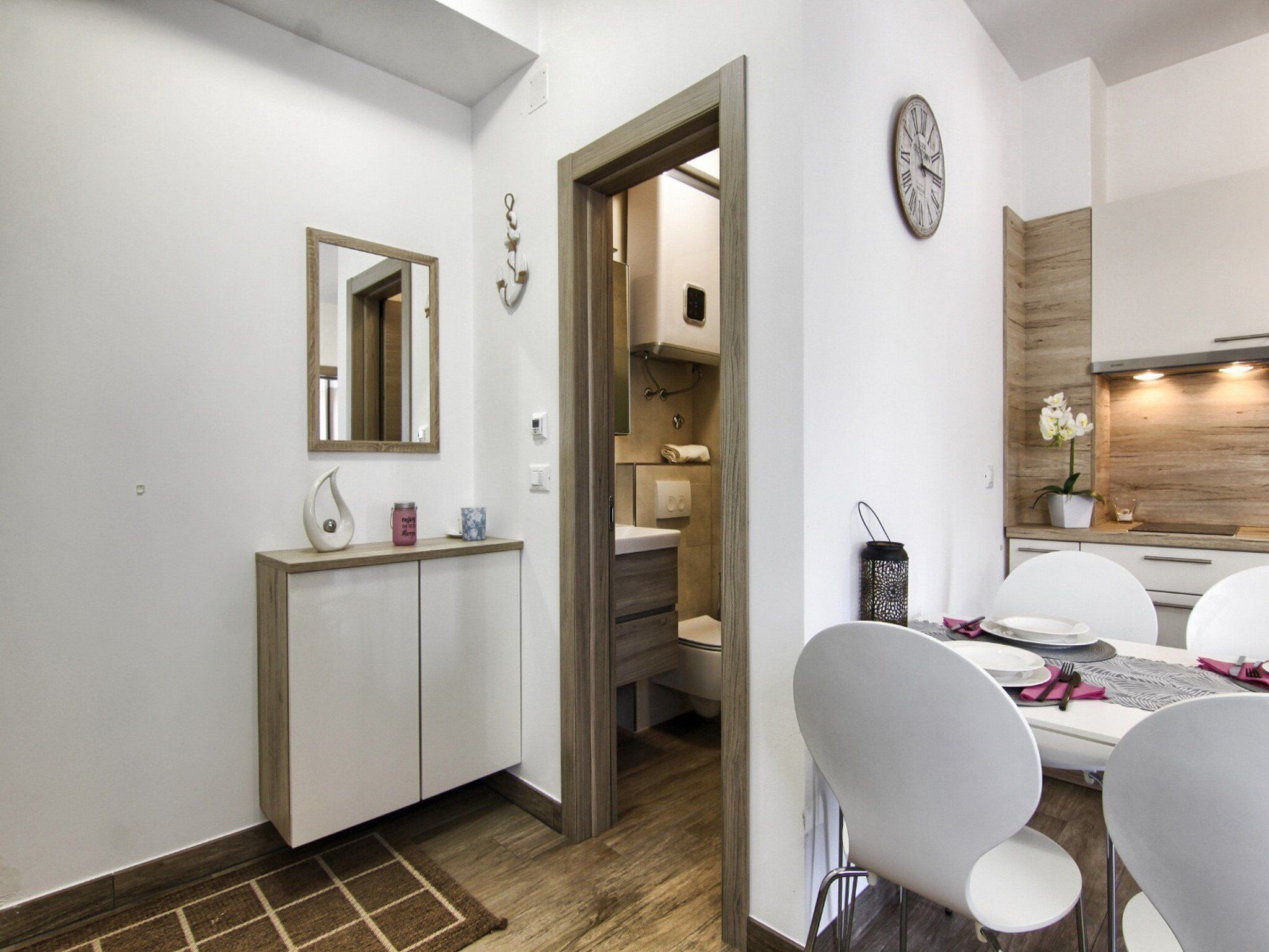 A modern kitchen with white cabinets, a wooden countertop, and a dining area with white chairs and a table set for two.