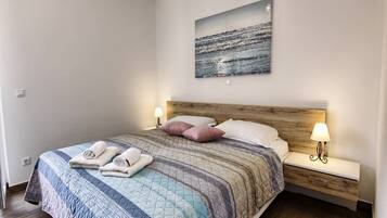 Een net opgemaakt bed met een sprei, twee bedlampen en een schilderij erboven.