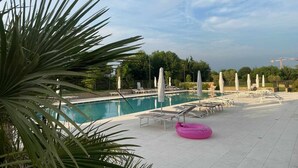 A swimming pool with lounge chairs and umbrellas, surrounded by palm trees and a clear sky.