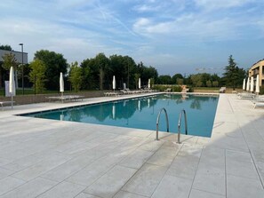A rectangular swimming pool with a tiled deck, surrounded by lounge chairs and umbrellas. - Apartment Garden Borgo Secolo with Private Garden & Wi-Fi (Peschiera del garda)