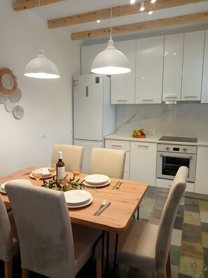 A modern kitchen with white cabinets, a wooden dining table set for two, and a built-in oven.