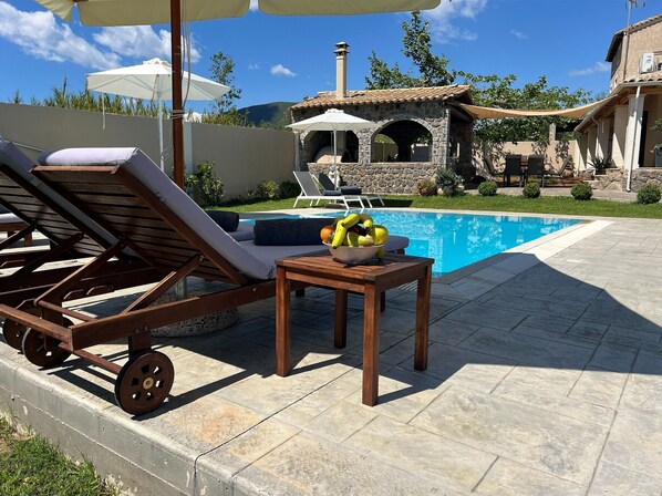 A poolside area with lounge chairs, a table with fruit, and a stone building in the background.