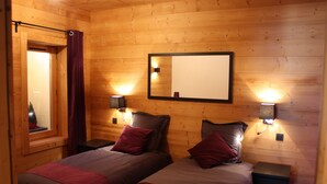 A wooden cabin bedroom with two beds, a mirror, and wall-mounted lights.