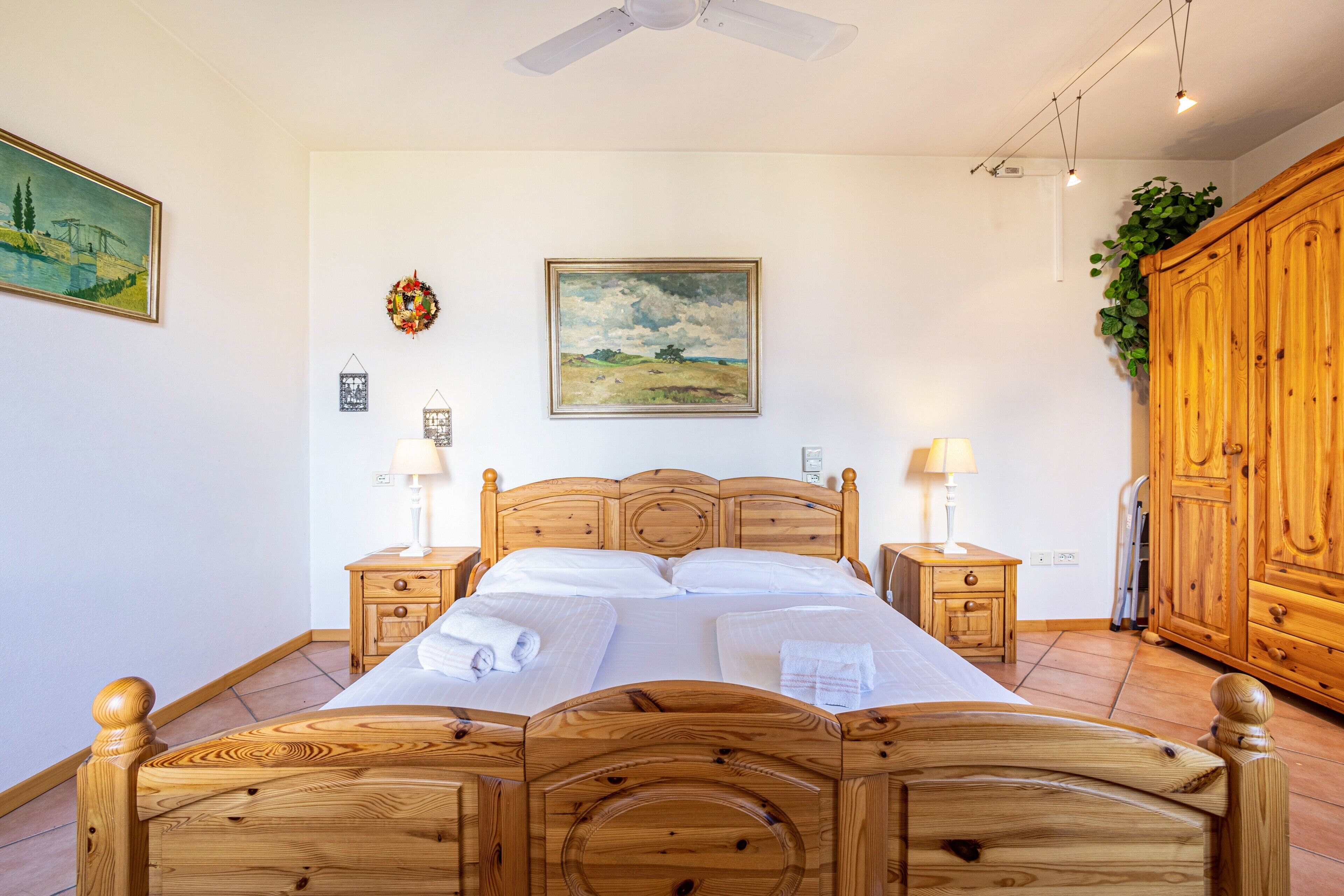 Ein Bett mit Holzkopfteil, zwei Nachttische mit Lampen, ein Bild an der Wand und ein Holzschrank.