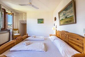 Une chambre à coucher avec deux lits en bois, un ventilateur de plafond, un tableau et une vue sur l’extérieur.