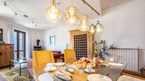 Een eetruimte met een glazen tafel, rieten stoelen en hangende hanglampen.