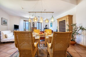 Un coin repas avec des chaises en osier, une table en verre et des lampes suspendues.