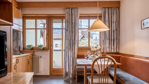 Una stanza accogliente con un tavolo da pranzo in legno, sedute a panchina, una televisione e un'ampia finestra con tende.
