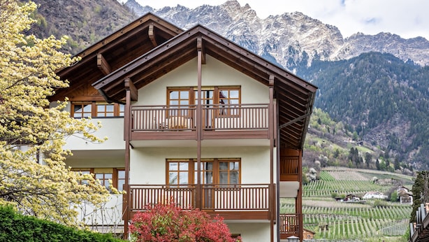 Un edificio a due piani con balconi, immerso tra montagne e vigneti.