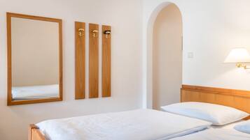 A hotel room with a bed, a mirror, and three wooden wall-mounted hooks.