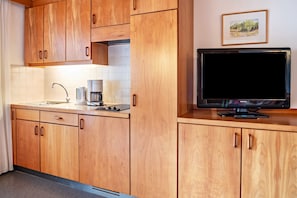 A kitchen with wooden cabinets, a sink, a coffee maker, and a television on a wooden counter.