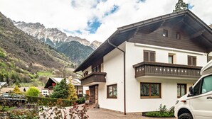 Um edifício moderno de dois andares com varanda, calçada e paisagem montanhosa ao fundo.