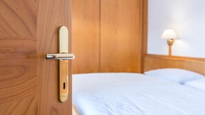 Una puerta de madera con manija, una cama con ropa blanca y una lámpara sobre una mesita de noche.