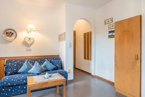 A room with a blue patterned sofa, a wooden table, a wall-mounted lamp, and a wooden wardrobe.