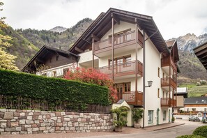 Un hôtel à plusieurs étages, doté de balcons, d’un mur en pierre et surplombant un paysage montagneux.
