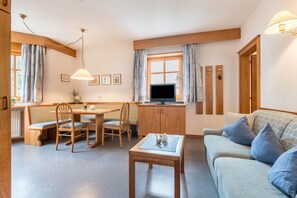 A cozy living room with a sofa, a dining table with chairs, a television, and wooden cabinets.