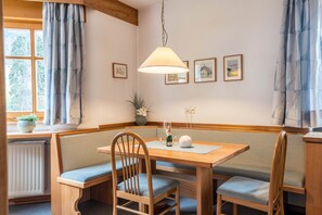 Un coin repas avec une table en bois, des bancs, un luminaire suspendu, des tableaux encadrés au mur et une fenêtre avec des rideaux.