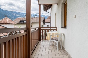 Un balcon avec une balustrade en bois, une table blanche agrémentée d’un coussin et une vue sur des montagnes enneigées.