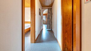 Un estrecho pasillo con paredes y techo de madera, que conduce a una habitación con una cama.